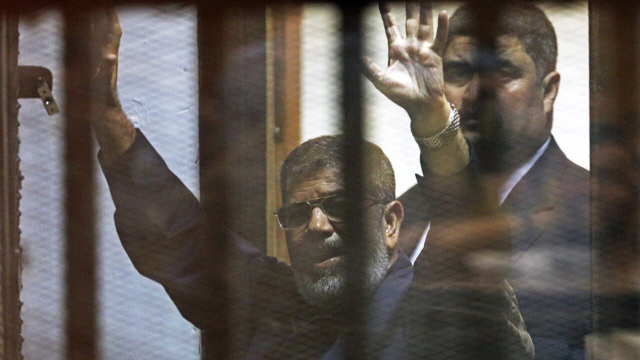 EGYPT-MURSI/ Deposed Egyptian President Mohamed Mursi greets his lawyers and people from behind bars after his verdict at a court on the outskirts of Cairo, Egypt June 16, 2015. An Egyptian court sentenced deposed President Mohamed Mursi to death on Tuesday on charges of killing, kidnapping and other offences during a 2011 mass jail break.The general guide of the Muslim Brotherhood, Mohamed Badie, and four other Brotherhood leaders were also handed the death penalty. More than 80 others were sentenced to death in absent