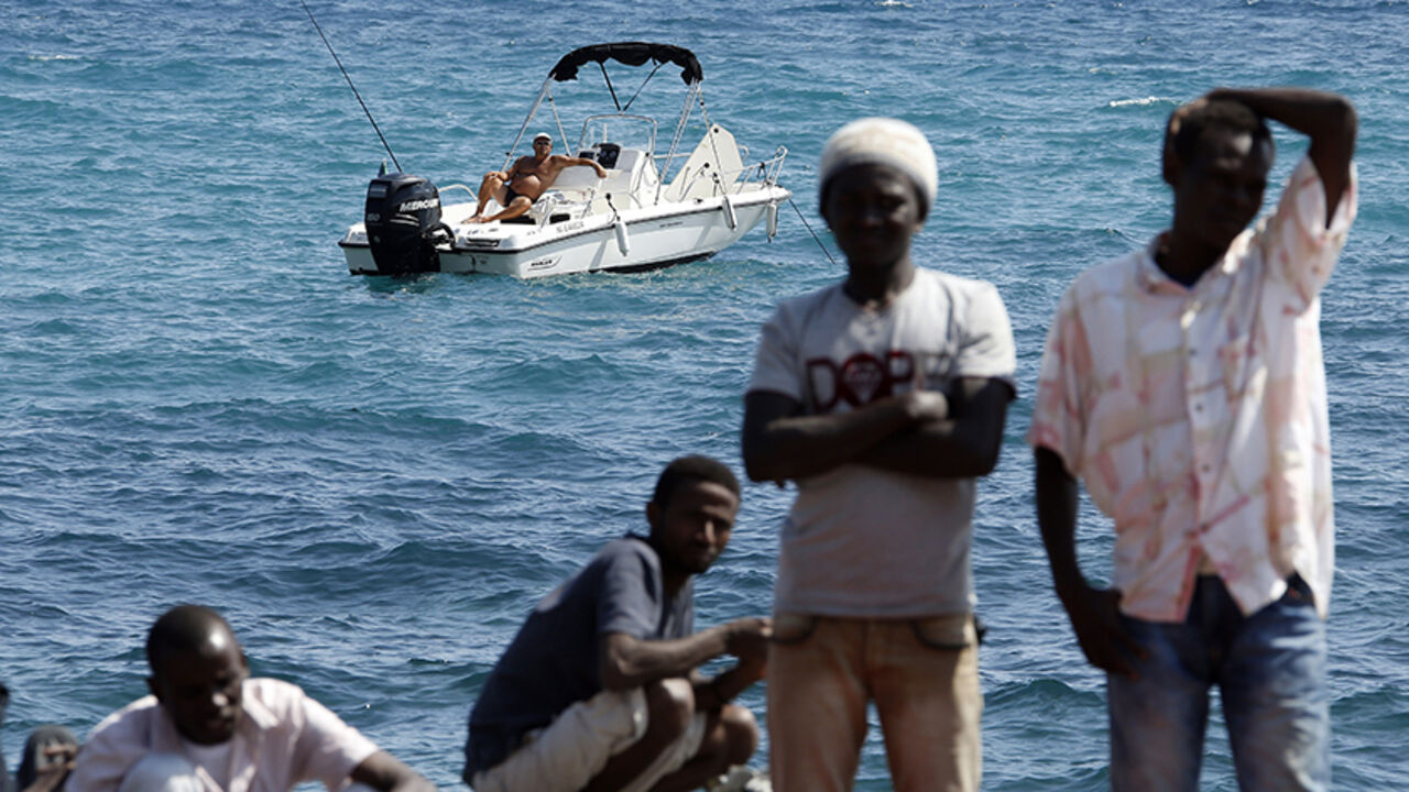 EUROPE-MIGRANTS/ A man fishes from his boat as a group of migrants gather on the seawall at the Saint Ludovic border crossing on the Mediterranean Sea between Vintimille, Italy and Menton, France, June 14, 2015. On Saturday, some 200 migrants, principally from Eritrea and Sudan who attempted to cross the border, were blocked by Italian police and French gendarmes. REUTERS/Eric Gaillard TPX IMAGES OF THE DAY - RTX1GFZS