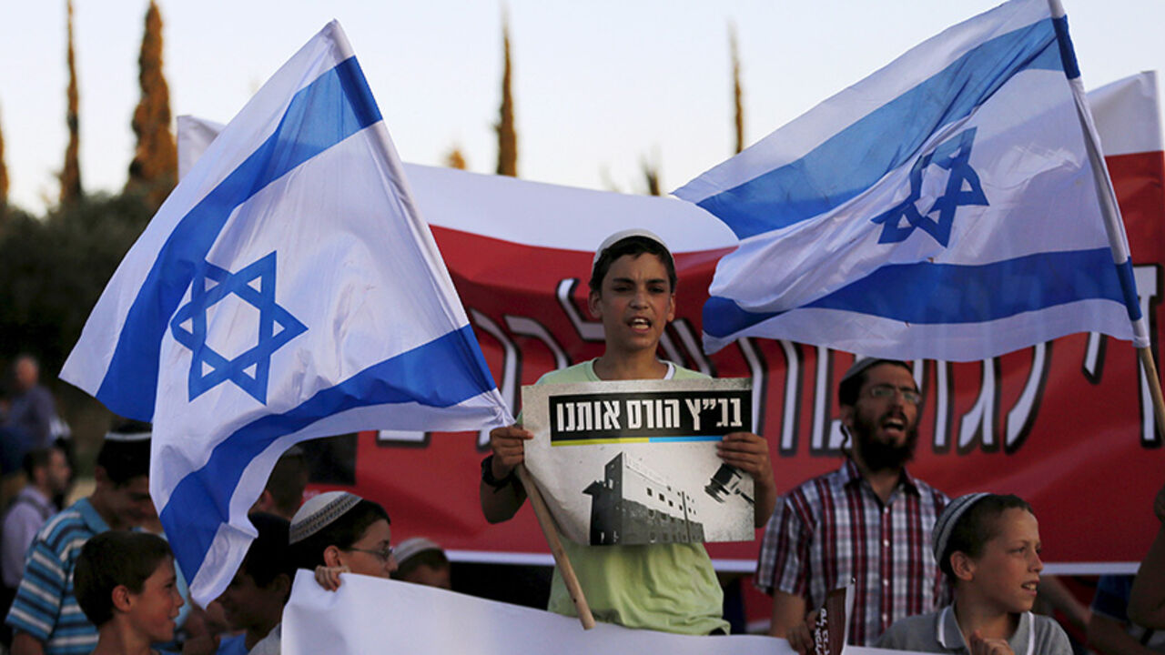 ISRAEL-PROTEST/ An Israeli protester holds a placard and a flag during a demonstration against a court decision to demolish housing units in the Jewish settlement of Beit El, outside the Supreme Court in Jerusalem July 8, 2015. Israel's Supreme Court ruled that 24 housing units, built on Palestinian owned land, be razed by July 30, according to local media. The placard in Hebrew reads, "The Supreme Court is ruining us". REUTERS/Ammar Awad - RTX1JMGQ