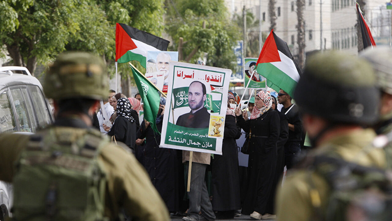 PALESTINIAN-ISRAEL/ Israeli soldiers stand guard as Palestinians hold national flags and posters of jailed relatives during a protest in solidarity with prisoners on hunger strike,in the West Bank city of Hebron June 4, 2014. Some 120 Palestinians jailed without trial in Israel have been on an open-ended hunger strike, eating only salt and drinking water, since April 24 to demand an end to so-called "administrative detention". REUTERS/Mussa Qawasma (WEST BANK - Tags: POLITICS CIVIL UNREST) - RTR3S7JN