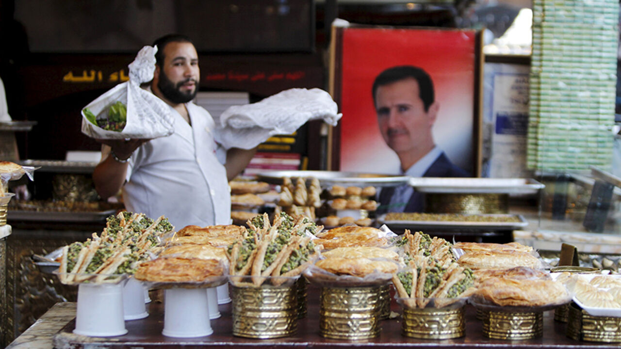 RELIGION-RAMADAN/ A vendor sells traditional sweets near a picture of Syria's President Bashar al-Assad during the Muslim fasting month of Ramadan in Damascus, Syria July 8, 2015. Picture taken July 8, 2015. REUTERS/Omar Sanadiki - RTX1JOL3