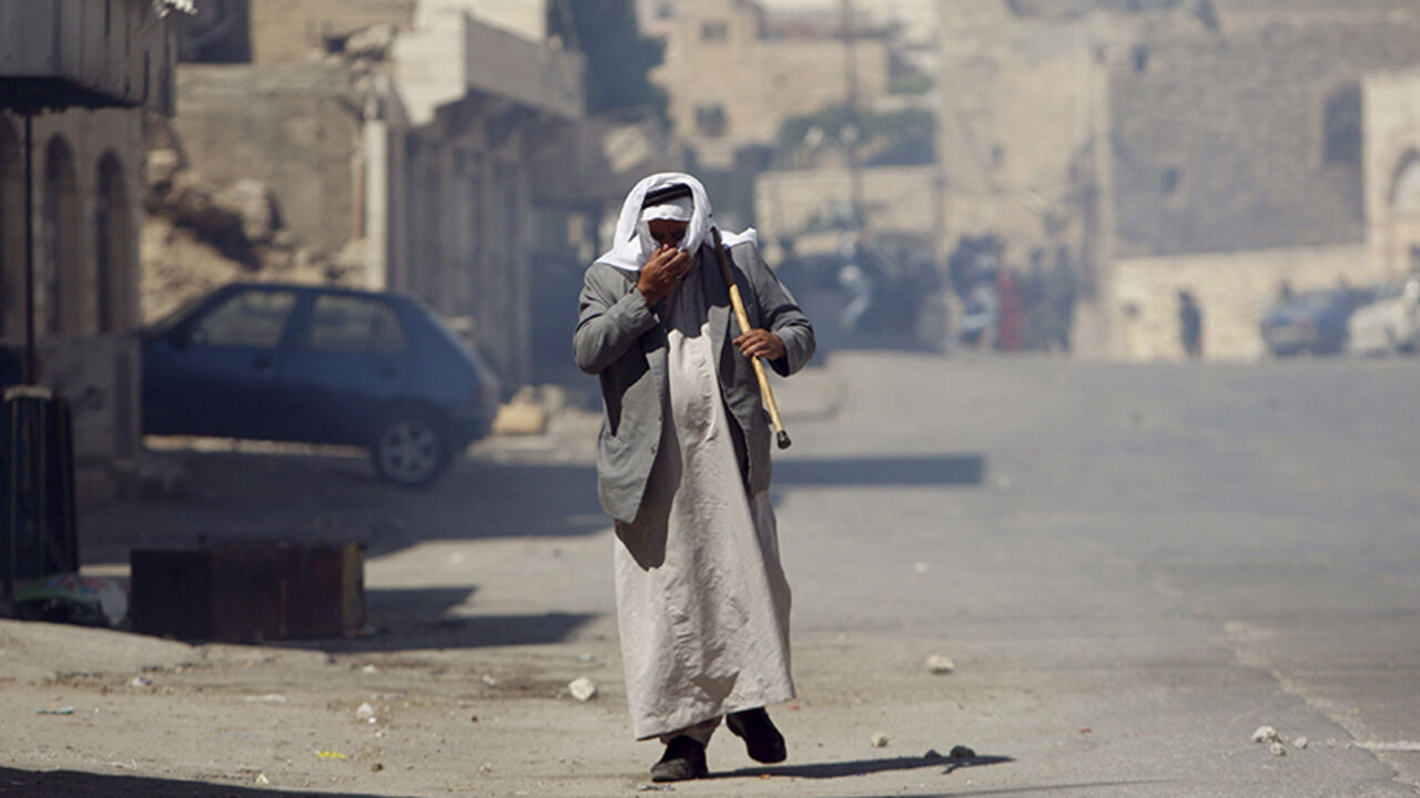 ISRAEL-PALESTINIANS/JERUSALEM A Palestinian man covers his face from tear gas fired by Israeli troops during clashes following a protest against the Israeli police raid on Jerusalem's al-Aqsa mosque on Tuesday, in the occupied West Bank city of Hebron September 18, 2015. Israel deployed hundreds of extra police around the Old City of Jerusalem on Friday after Palestinian leaders called for a 'day of rage' to protest at new Israeli security measures. REUTERS/Mussa Qawasma - RTS1R5M
