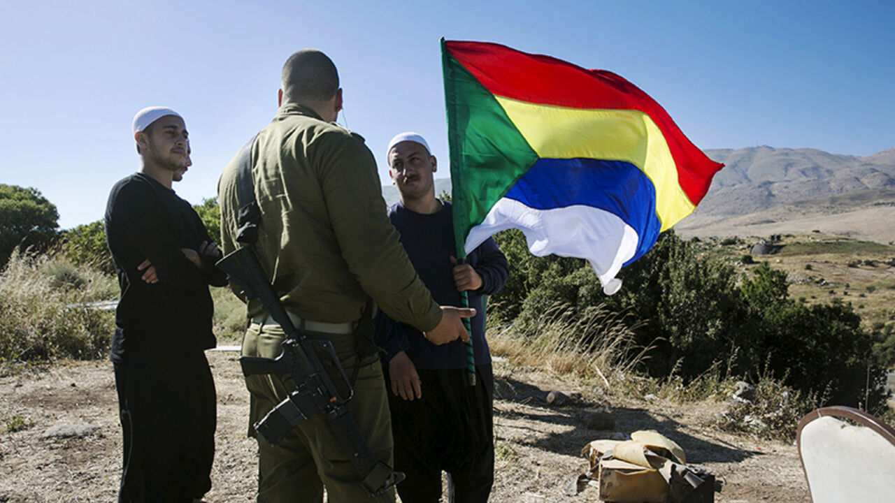 ISRAEL-SYRIA/DRUZE A member of the Druze community holds a Druze flag as he speaks to an Israeli soldier near the border fence between Syria and the Israeli-occupied Golan Heights, near Majdal Shams June 18, 2015. Gathered at a hilltop in the Israeli-held Golan Heights, a group of Druze sheikhs look through binoculars at the Syrian village of Hader, surrounded by Islamist fighters. They fear their brethren are in imminent danger. Intense battles this week have left Syria's al Qaeda branch, the Nusra Front, in control of hills