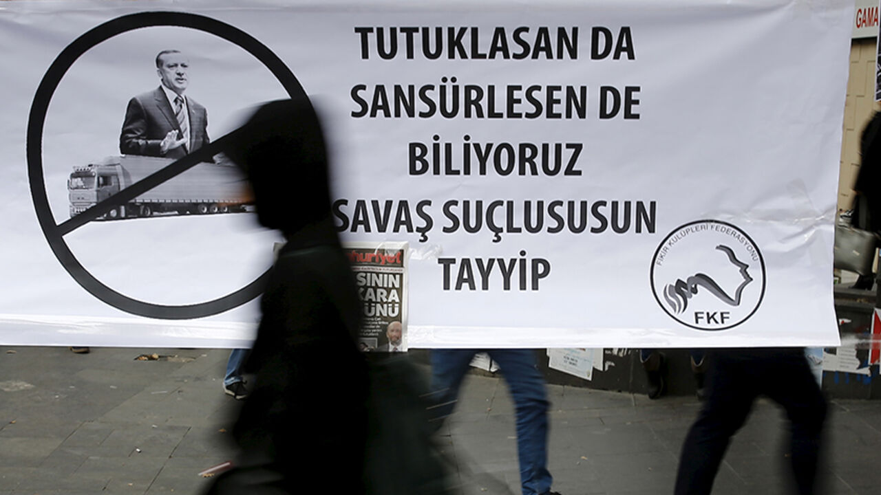 A woman walks past a banner that reads, "Even you arrest (journalists) or censor (media) we know that you are a war criminal Tayyip" and with a picture of Turkish President Recep Tayyip Erdogan during a protest over the arrest of journalists Can Dundar and Erdem Gul in Ankara, Turkey, November 27, 2015. Around 2,000 people protested on Friday over the arrest of two prominent journalists on charges of espionage and terrorist propaganda, a case that has revived long-standing criticism of Turkey's record on pr