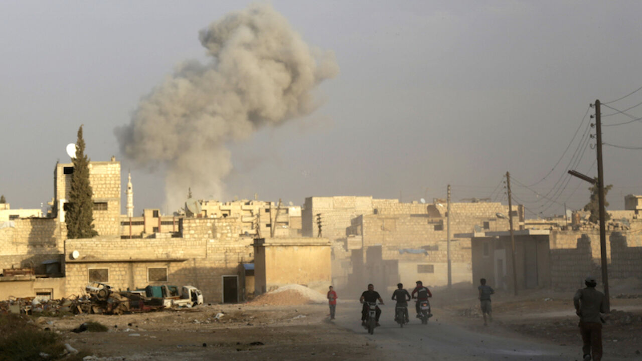 MIDEAST-CRISIS/SYRIA-RUSSIA Men ride motorcycles as smoke rises because of, what activists said was, an airstrike carried out by the Russian air force in the rebel-controlled area of Maaret al-Numan town in Idlib province, Syria October 24, 2015. REUTERS/Khalil Ashawi - RTS7RYZ