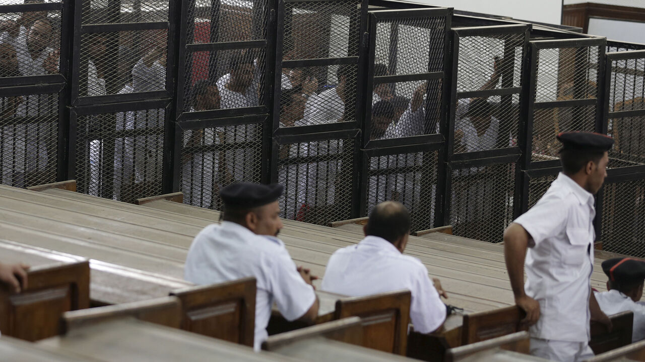 EGYPT-RIGHTS/ Suhayb Saad, an activist who rights groups say was taken by security forces and forced to confess on TV his membership of a terrorist cell, a reference to the Muslim Brotherhood, stands behind bars with other co-defendants as they wait to listen the ruling at a court in Cairo June 23, 2014. Picture taken June 23, 2014. To match EGYPT-RIGHTS/ REUTERS/Asmaa Waguih - RTX1OSZH