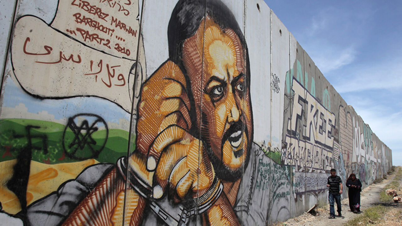 ISRAEL-PALESTINIANS-NETANAYHU/ Palestinians walk past graffiti depicting jailed Fatah leader Marwan Barghouti on a section of the controversial Israeli barrier near the Qalandiya checkpoint outside the West Bank city of Ramallah May 25, 2011. Palestinians and Israelis alike saw little prospect of a fresh start to Middle East peace talks on Wednesday after Israeli Prime Minister Benjamin Netanyahu's keynote speech to Congress. REUTERS/Baz Ratner (WEST BANK - Tags: POLITICS) - RTR2MVS6