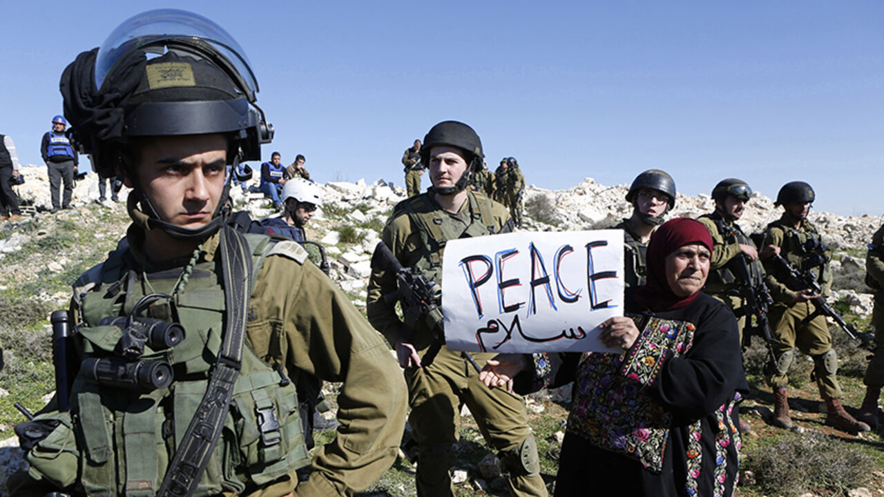 MEDEAST-PALESTINIANS-ISRAEL A protester holds a placard as she stands next to Israeli soldiers during a protest against Israeli settlements in Beit Fajjar town south of the West Bank city of Bethlehem December 27, 2014. REUTERS/ Mussa Qawasma (WEST BANK - Tags: POLITICS CIVIL UNREST TPX IMAGES OF THE DAY) - RTR4JDTT