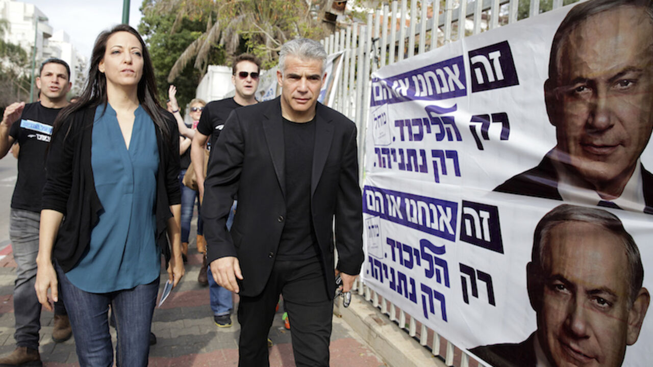 ISRAEL-ELECTION/ Yesh Atid leader Yair Lapid (R) and his wife Lihi walk past Likud election campaign posters depicting Israeli Prime Minister Benjamin Netanyahu as they walk to a polling station in Tel Aviv March 17, 2015. Netanyahu's march towards becoming the longest-serving leader of Israel could be halted on Tuesday in an election that has exposed public fatigue with his stress on national security rather than socio-economic problems. Once a heartthrob television news anchor, Lapid, 51, was the rising star of Israeli po