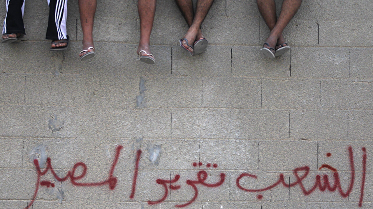 BAHRAIN-PROTEST/ Shi'ite Bahraini men sit on a wall with graffiti that reads ''People want self-determination", as they attend a rally held by the Wefaq opposition party, in the village of Boori, south of Manama, October 14, 2011, to mark the 8-month anniversary of the February 14 uprising. REUTERS/Hamad I Mohammed (BAHRAIN - Tags: CIVIL UNREST POLITICS) - RTR2SO9O