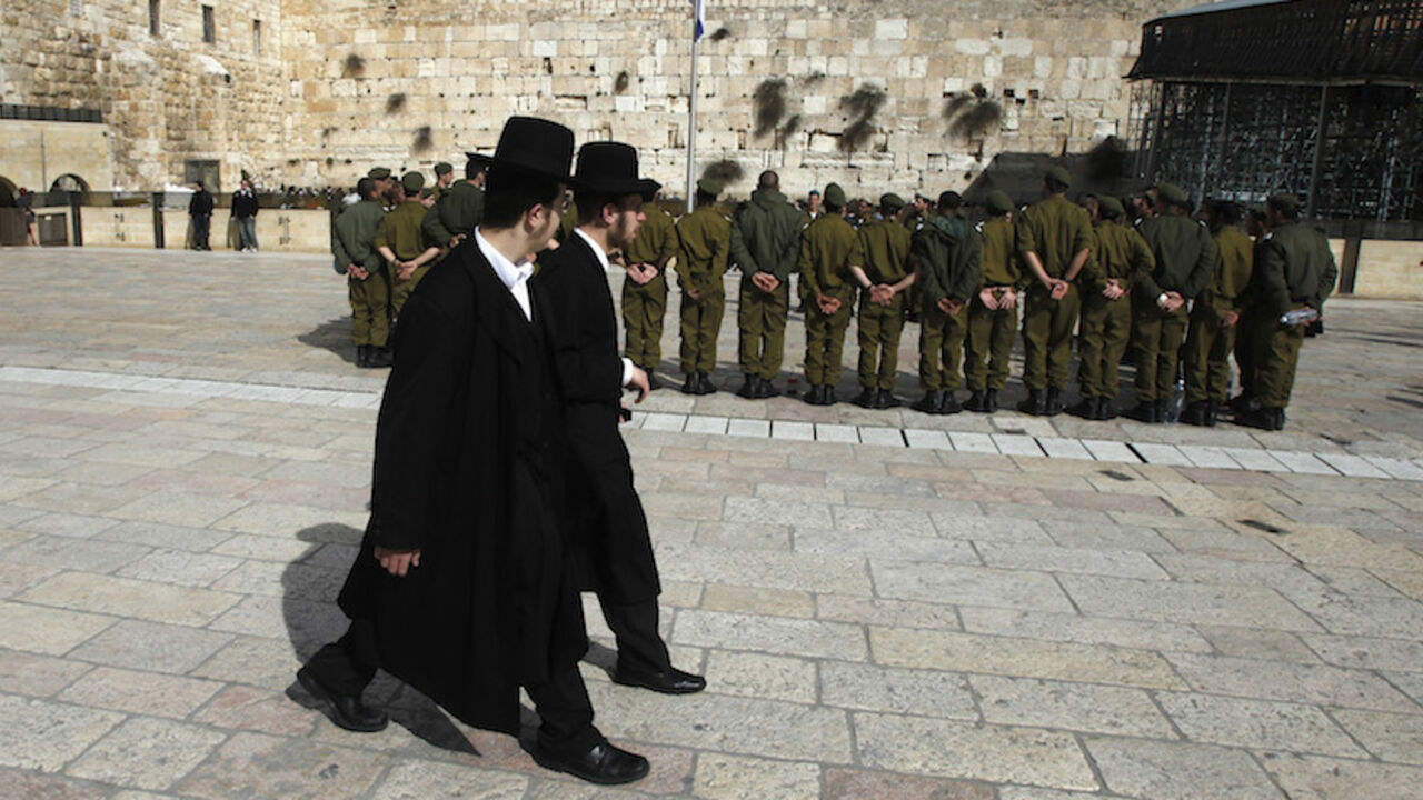 To match Insight ISRAEL/RELIGION-IDF Ultra-Orthodox Jewish men walk behind Israeli soldiers at the Western Wall, Judaism's holiest prayer site, in Jerusalem's Old City February 22, 2012. The Israeli Defence Force (IDF) has always been a 'Jewish' army. Its rations are kosher, its chaplains are rabbis, and it operates - with the exception of wartime - around the festival calendar. It has never drafted soldiers from Israel's 20-percent Arab minority. But its Jewish identity has always been more cultural than religious. IDF personnel data suggests