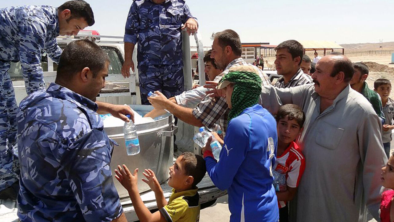 Nic6359507 Iraqi military personnel distribute water to Shiite Iraqi Kurds, known as "Shabak", displaced by fierce fighting between Kurdish peshmerga forces and jihadist militants from the Islamic State (IS) after arriving on the road between Kirkuk and Arbil having fled the area of Bartala near the northern Iraqi city of Mosul, on August 8, 2014. Jihadists seized Iraq's largest dam north of their hub of Mosul, giving them control over the supply of water and electricity for a vast area, officials said. AFP PHOTO / MA