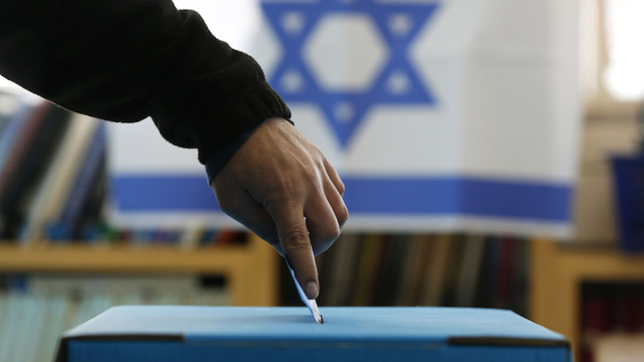 An Israeli flag is seen in the background as a man casts his ballot at a polling in a West Bank Jewish settlement, north of Ramallah An Israeli flag is seen in the background as a man casts his ballot for the parliamentary election at a polling in the West Bank Jewish settlement of Ofra, north of Ramallah January 22, 2013. Israelis voted on Tuesday in an election that is expected to see Prime Minister Benjamin Netanyahu win a third term in office, pushing the Jewish state further to the right, away from peace with the Palestinians and towards a showdown with Iran. REUTERS/Baz Ratner (WEST BANK - Tags: POLITICS ELECTIONS TPX IMAGES OF THE