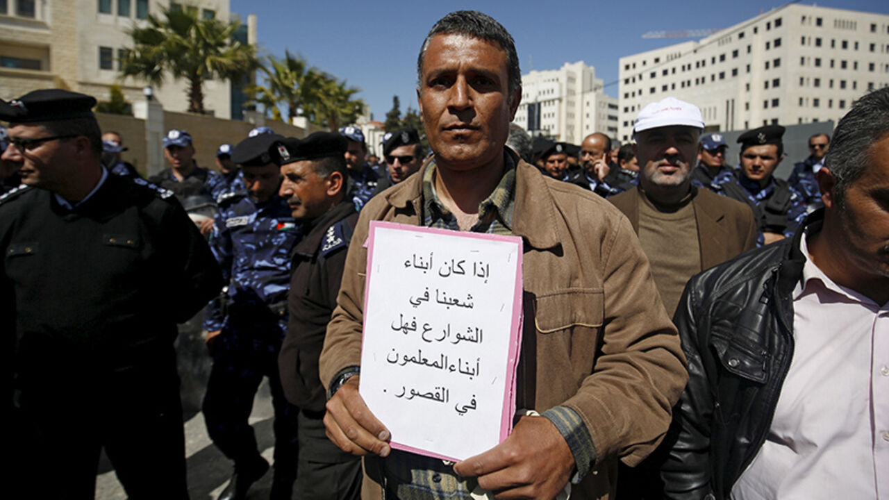 PALESTINIANS-TEACHERS/ A Palestinian teacher holds a sign during a protest demanding better pay and conditions, in the West Bank city of Ramallah March 7, 2016. For a month, more than 25,000 teachers in the West Bank have been on strike over pay and benefits, causing chaos for schools, pupils and parents, and prompting the Palestinian Authority to deploy military police on the streets of Ramallah. The sign reads, "If the sons of our people are in the streets, are the teachers' sons in palaces?". Picture taken March 7. REUTERS/Moh
