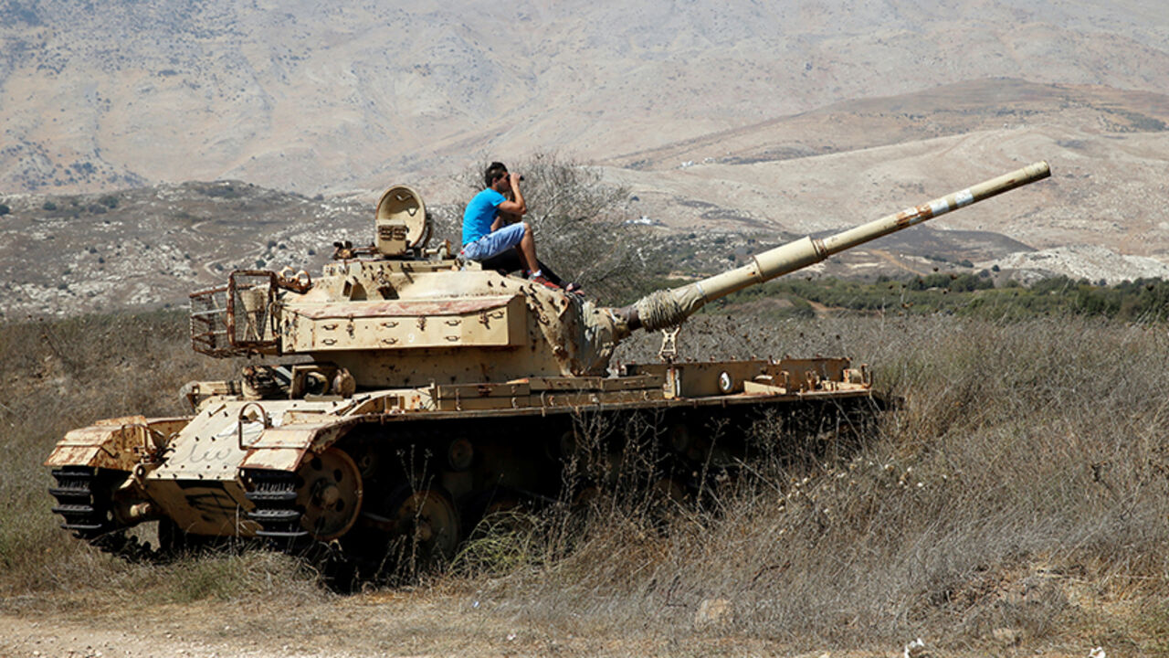MIDEAST-CRISIS/SYRIA-ISRAEL A man sits on an old tank as he watches fighting taking place in Syria as seen from the Israeli side of the border fence between Syria and the Israeli-occupied Golan Heights September 11, 2016. REUTERS/Baz Ratner - RTSN7X9