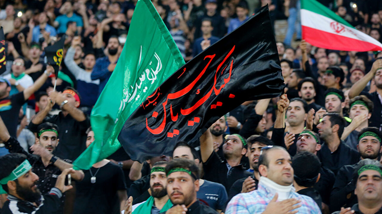 AFP_H21BN Iranian fans wave a religious banner to mark Ashura, which marks the death of Prophet Mohammed's grandson Imam Hussein in the seventh century, during the 2018 World Cup qualifying football match between Iran and South Korea at the Azadi Stadium in Tehran on October 11, 2016. / AFP / ATTA KENARE (Photo credit should read ATTA KENARE/AFP/Getty Images)