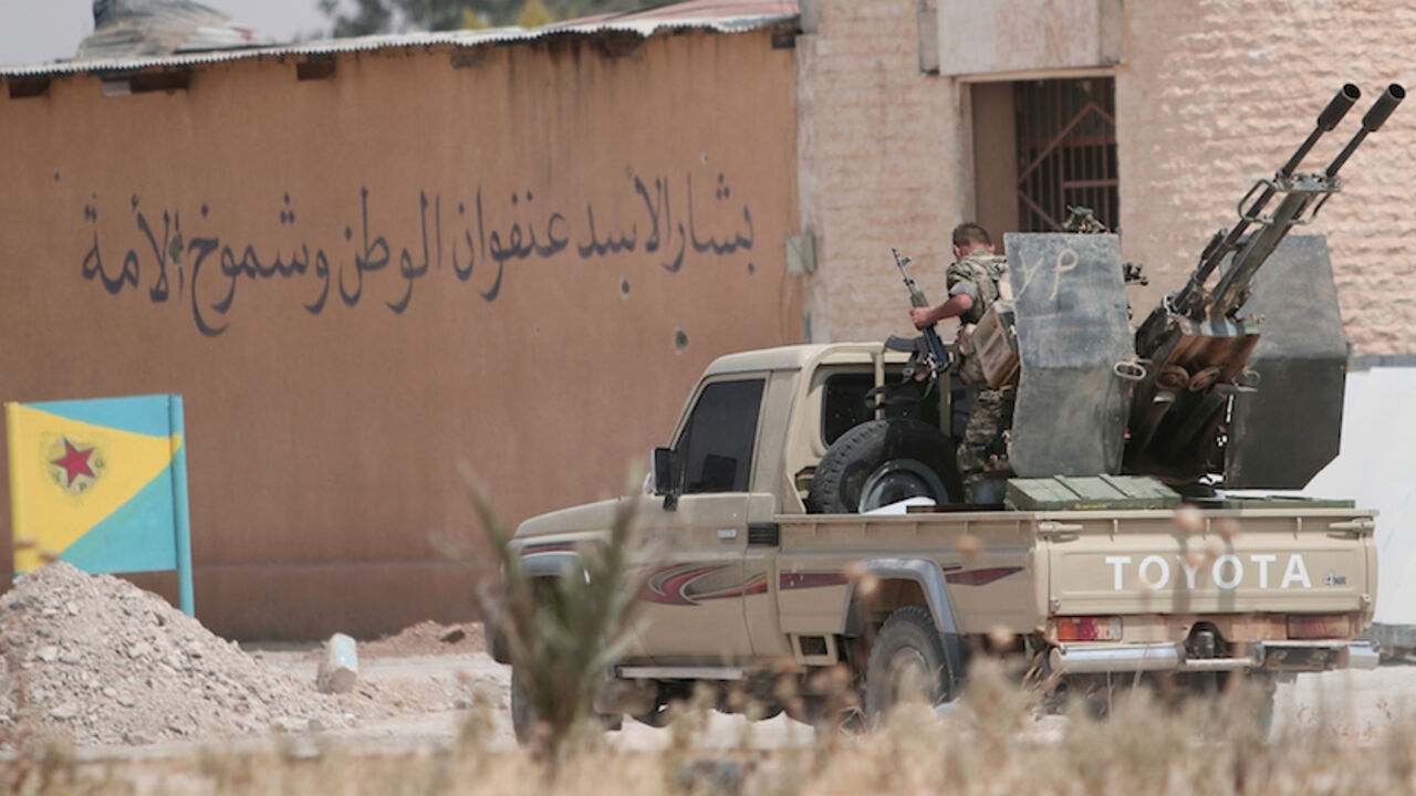 MIDEAST-CRISIS/SYRIA-HASAKA A Kurdish fighter from the People's Protection Units (YPG) rides on a pick-up truck mounted with an anti-aircraft weapon in the Ghwairan neighborhood of Hasaka, Syria, August 22, 2016. The Arabic on the wall reads, "Bashar al-Assad is the glory and the pride of the nation." REUTERS/Rodi Said - RTX2MKNY