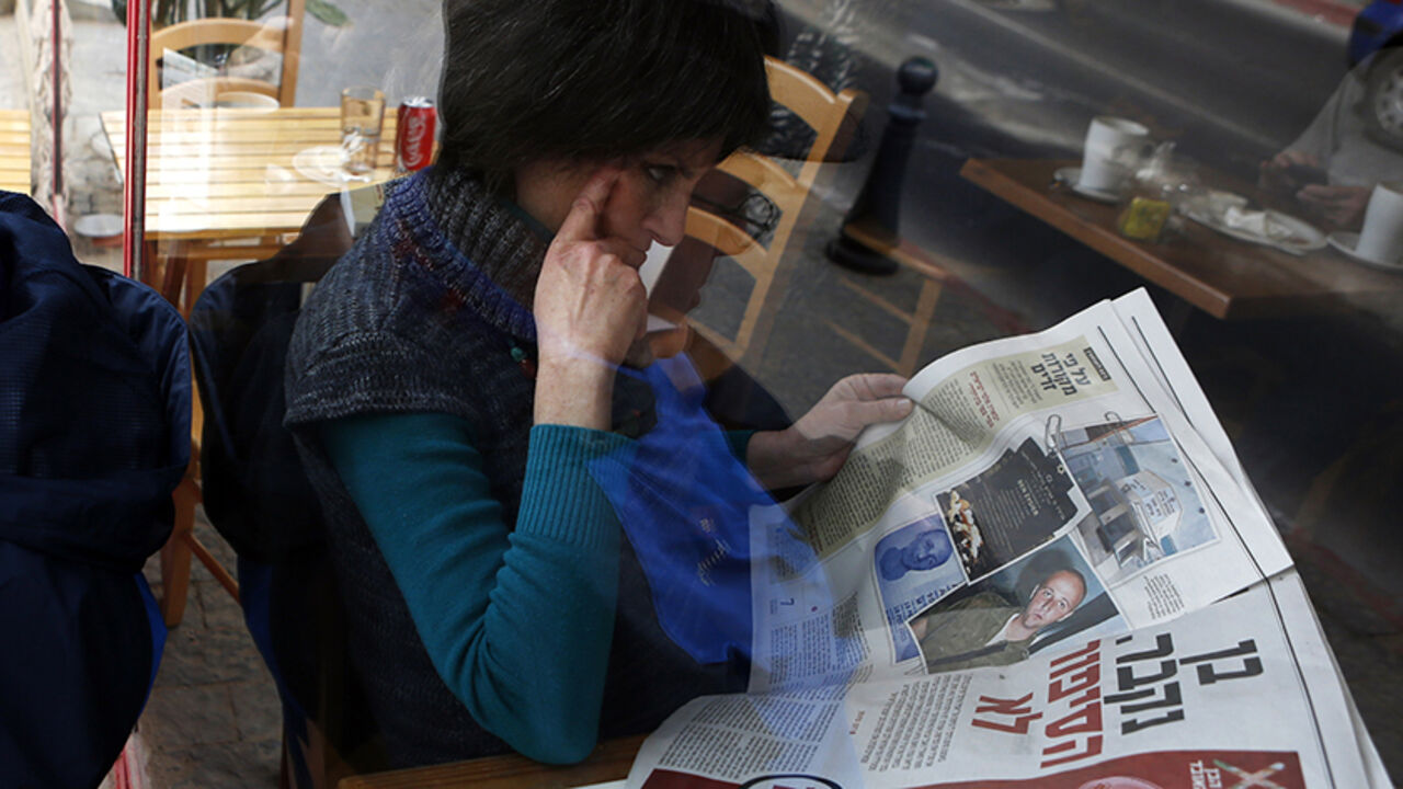 ISRAEL-AUSTRALIA/SPY A woman is seen through a coffee shop window as she reads an article about Ben Zygier in an Yedioth Ahronoth newspaper in Jerusalem February 15, 2013. Zygier, the Australian immigrant reported to have been recruited by Israel's Mossad spy agency, was charged with grave crimes before he committed suicide in an Israeli jail, one of his lawyers said on Thursday. REUTERS/Baz Ratner (JERUSALEM - Tags: POLITICS CRIME LAW) - RTR3DTPG