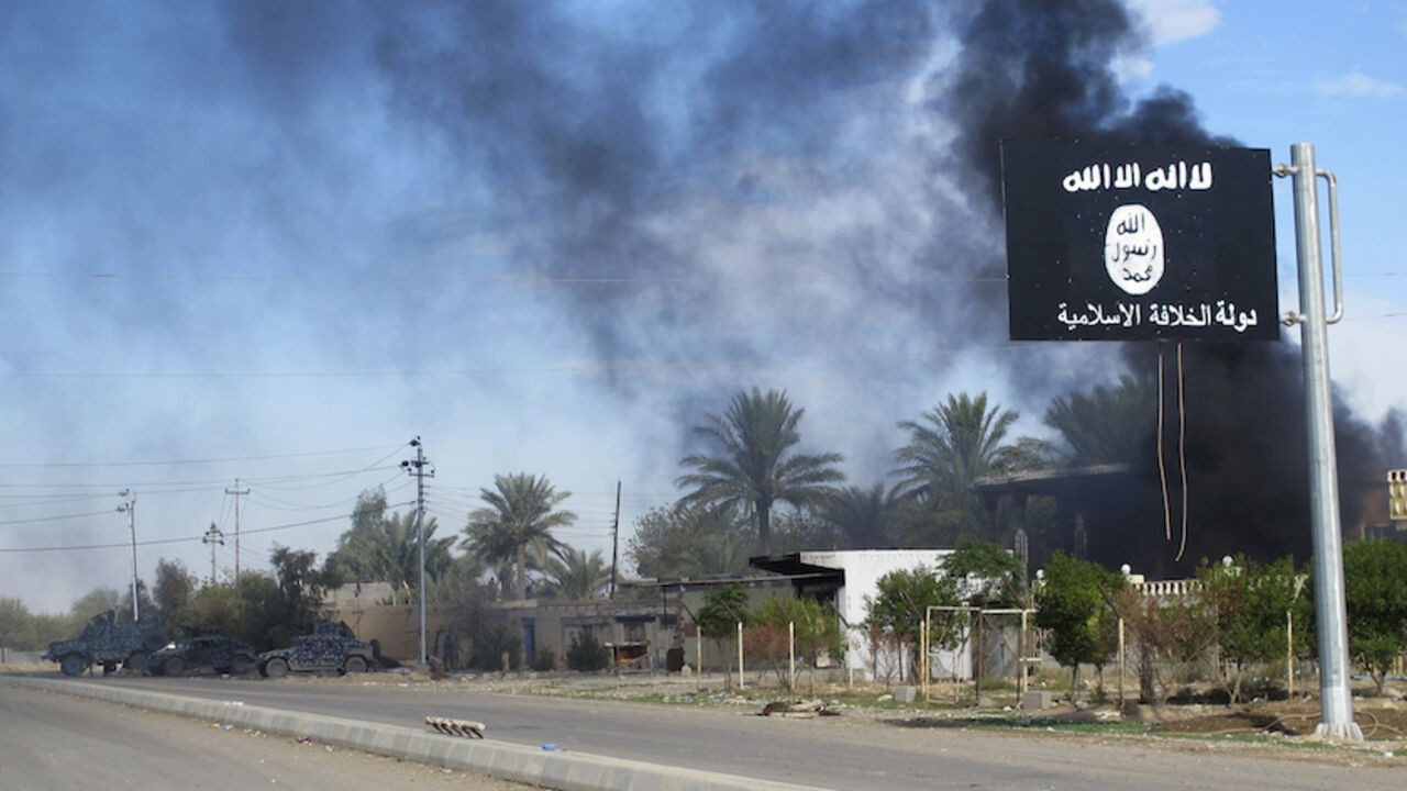 MIDEAST-CRISIS/IRAQ-TOWNS Smoke raises behind an Islamic State flag after Iraqi security forces and Shiite fighters took control of Saadiya in Diyala province from Islamist State militants, November 24, 2014. Iraqi forces said on Sunday they retook two towns north of Baghdad from Islamic State fighters, driving them from strongholds they had held for months and clearing a main road from the capital to Iran. There was no independent confirmation that the army, Shi'ite militia and Kurdish peshmerga forces had completely retaken Jalawl