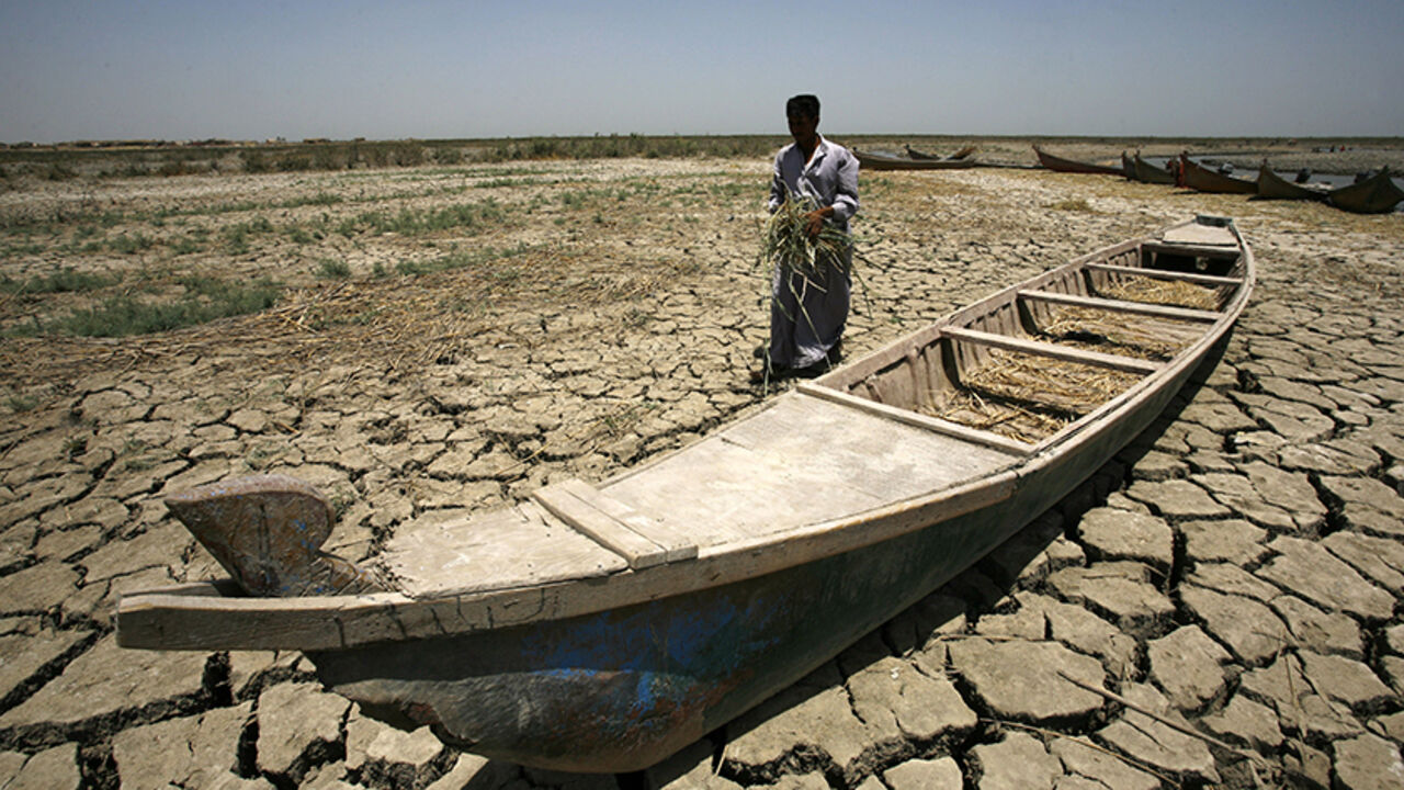 Nic6464028 An Iraqi man walks past a canoe siting on dry, cracked earth in the Chibayish marshes near the southern Iraqi city of Nasiriyah on June 25, 2015. Marsh areas in southern Iraq have been affected since the Islamic State group started closing the gates of a dam on the Euphrates River in the central city of Ramadi, which is under the jihadist group's control. AFP PHOTO / HAIDAR HAMDANI (Photo credit should read HAIDAR HAMDANI/AFP/Getty Images)