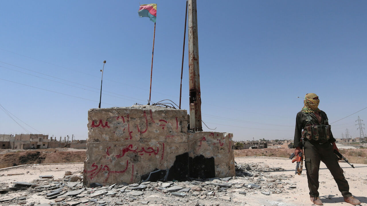 MIDEAST-CRISIS/SYRIA-KURDS A Kurdish fighter stands with his weapons near a fluttering Kurdish flag in the Ghwairan neighborhood of Hasaka, Syria, August 23, 2016.REUTERS/Rodi Said - RTX2MP4F