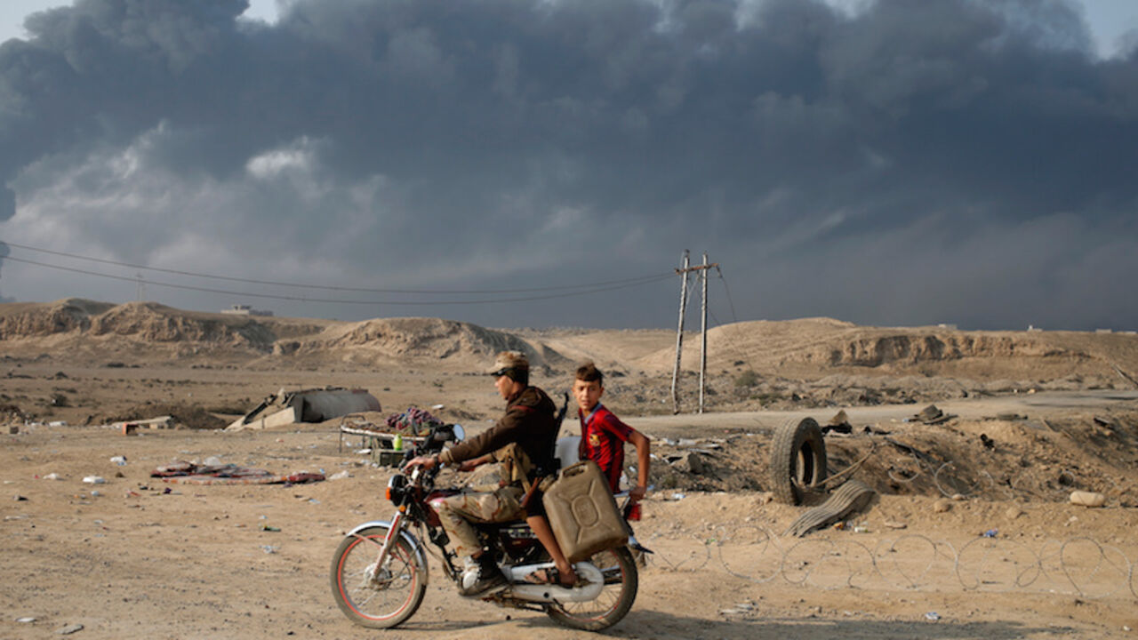 MIDEAST-CRISIS-IRAQ-MOSUL/ Armed members of Shi'ite militia Hashid Shaabi ride a motorbike near Qayyara, south of Mosul, Iraq October 27, 2016. Smoke in the background is from burning oilfields set ablazed by Islamic State fighters. REUTERS/Goran Tomasevic - RTX2QNPU