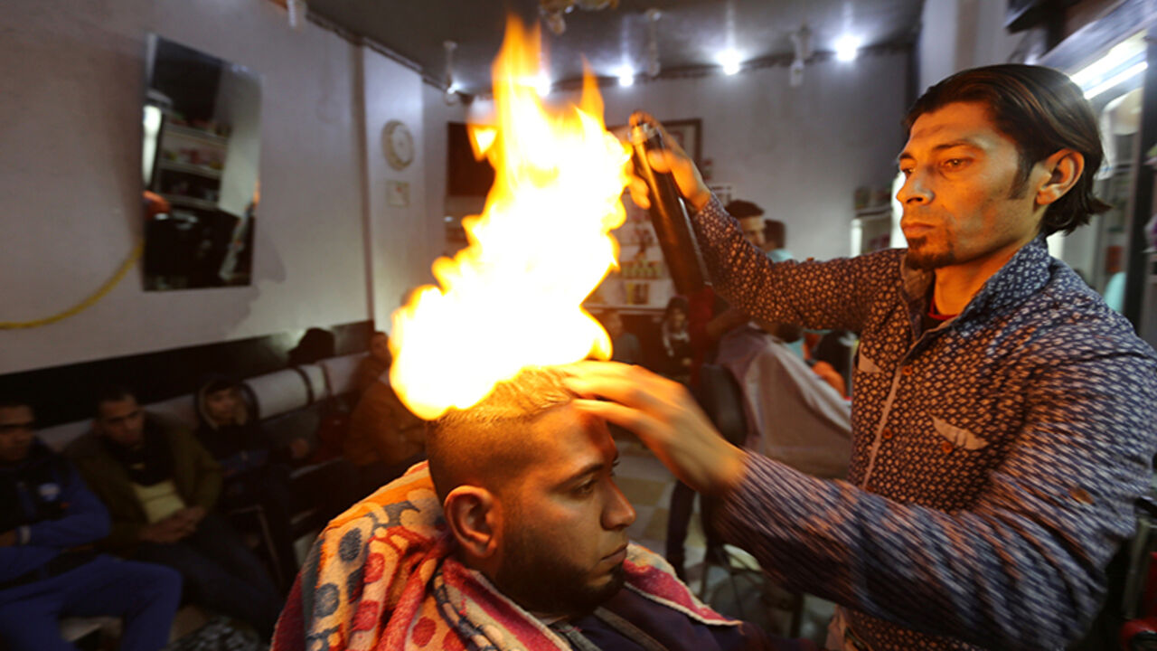PALESTINIANS-GAZA/HAIRDRESSER Palestinian barber Ramadan Odwan styles and straightens the hair of a customer with fire at his salon in Rafah, in the southern Gaza Strip February 2, 2017. Picture taken February 2, 2017. REUTERS/Ibraheem Abu Mustafa TPX IMAGES OF THE DAY - RTX309MG