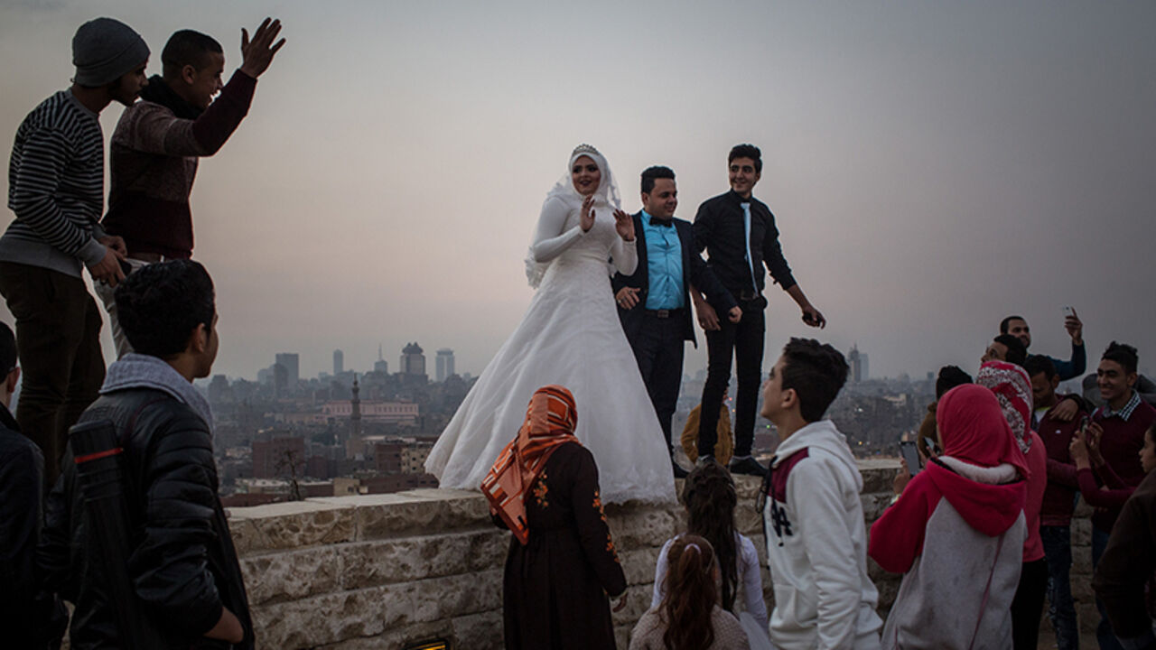 93870694 CAIRO, EGYPT - DECEMBER 10: A newlywed couple pose for wedding photos on a wall in a park overlooking Cairo on December 10, 2016 in Cairo, Egypt. Since the 2011 Arab Spring, Egyptians have been facing a crisis, the uprising brought numerous political changes, but also economic turmoil, increased terror attacks and the unravelling of the once strong tourism sector. In recent weeks Egypt has again been hit by multiple bomb blasts, the most recent killed 26 Christians inside the St Peter and St Paul Church dur