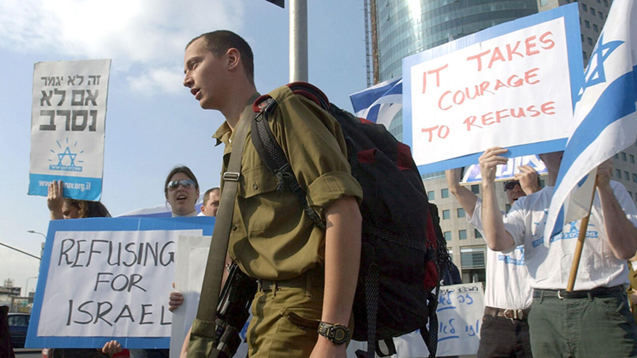 NIC2004031831341 An Israeli soldier passes a demonstration by left-wing Israelis calling on army recruits to refuse to serve in the Palestinian territories, as they protest outside the Defense Ministry in Tel Aviv 18 March 2004. AFP PHOTO/Tal COHEN (Photo credit should read TAL COHEN/AFP/Getty Images)