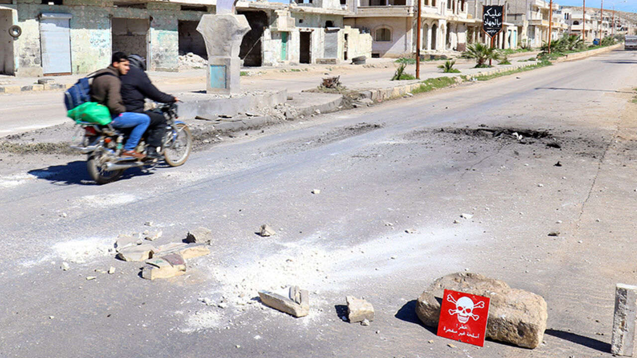MIDEAST-CRISIS/SYRIA-ATTACK Men ride a motorbike past a hazard sign at a site hit by an airstrike on Tuesday in the town of Khan Sheikhoun in rebel-held Idlib, Syria April 5, 2017. The hazard sign reads, "Danger, unexploded ammunition". REUTERS/Ammar Abdullah - RTX3475J