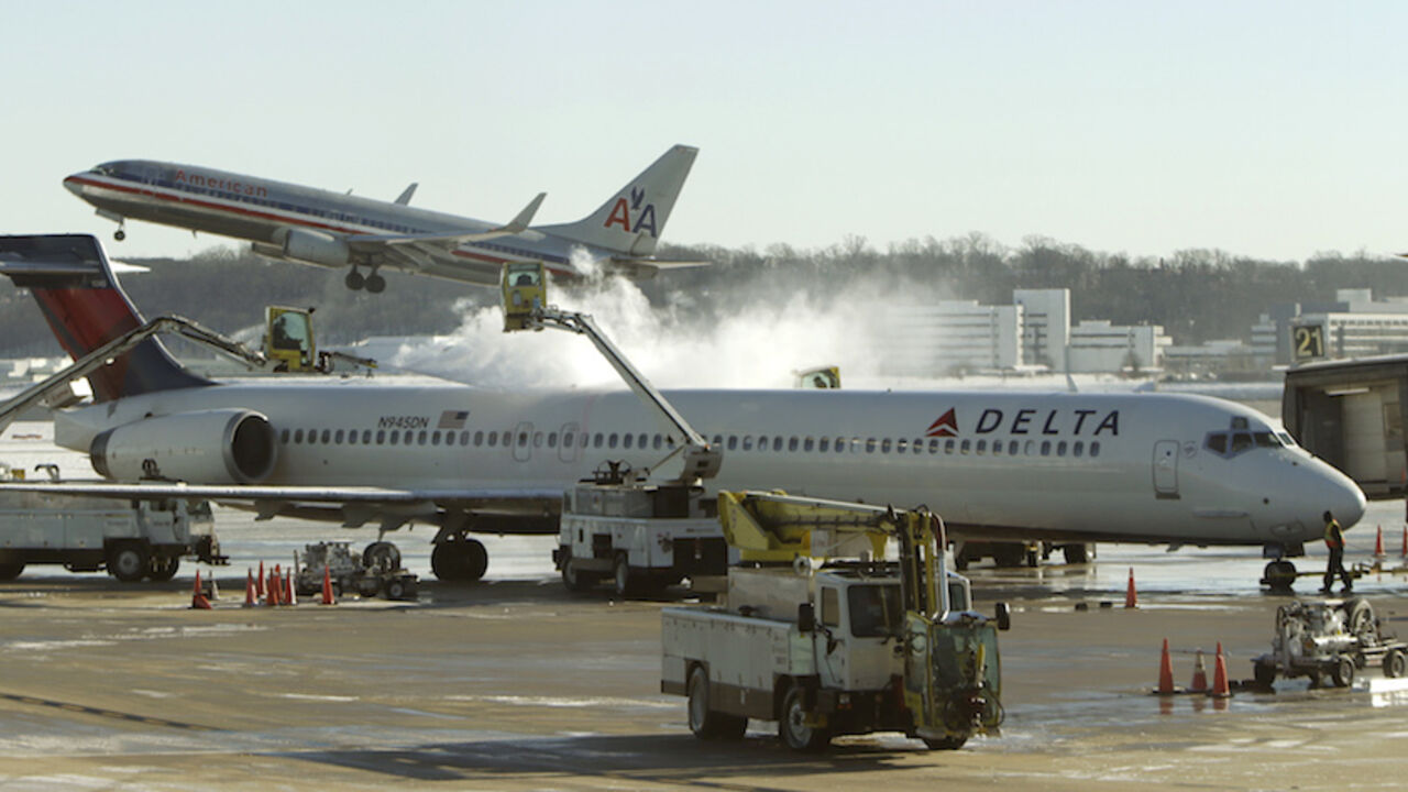 USA-WEATHER/ A Delta jetliner (foreground) is de-iced while an American Airlines plane (rear) takes off at Reagan National Airport in Washington January 3, 2014. A heavy snowstorm and dangerously cold conditions gripped the northeastern United States on Friday, delaying flights, paralyzing road travel and closing schools and government offices across the region. REUTERS/Gary Cameron (UNITED STATES - Tags: ENVIRONMENT TRANSPORT TRAVEL) - RTX1711Z