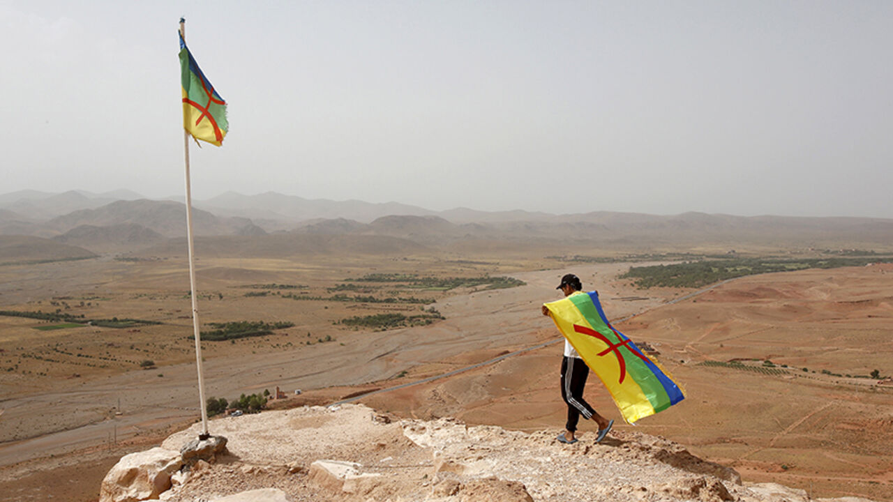 MOROCCO-ELECTIONS/ An activist carrying a Berber flag walks on a hilltop above a silver mine, where dozens of poor and unemployed young villagers have been holding a permanent sit-in since 2011, near the town of Imider, southeastern Morocco, August 31, 2015. They have cut off the flow of water from a well that supplies one of the biggest silver mines in Africa. Protesters want to make the company hire more locals and reconsider its water and environmental policies. Picture taken August 31, 2015. REUTERS/Youssef Boudlal - RTX1