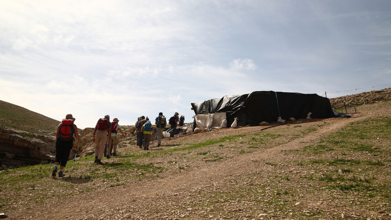 beduin_9459.jpg A line of hikers walk towards a semi-permanent, plastic-wrapped structure in a hillside, Bedouin nomad settlement , near Nachal (or Nahal Og), in the Judean Desert, West Bank, Israel, February 13, 2016. . (Photo by Dan Porges/Getty Images)