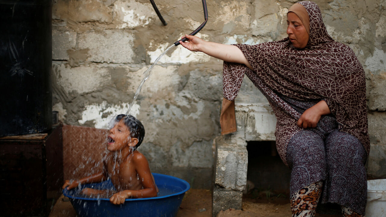 PALESTINIANS-GAZA/TEMPERATURE-POWER A Palestinian woman bathes her son with water from a tank, filled by a charity, inside their dwelling in Khan Younis, in the southern Gaza Strip, July 3, 2017. REUTERS/Mohammed Salem SEARCH "GAZA HEAT" FOR THIS STORY. SEARCH "WIDER IMAGE" FOR ALL STORIES. - RC1FC4354260