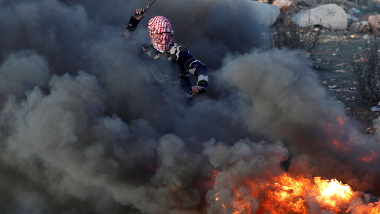 USA-TRUMP/ISRAEL-PALESTINIANS A masked Palestinian throws a stone at Israeli forces in front of a burned barricade during a protest against U.S. President Donald Trump's decision to recognize Jerusalem as the capital of Israel, near the Jewish settlement of Beit El, near the West Bank city of Ramallah December 11, 2017. REUTERS/Goran Tomasevic - RC1AAB56ECF0