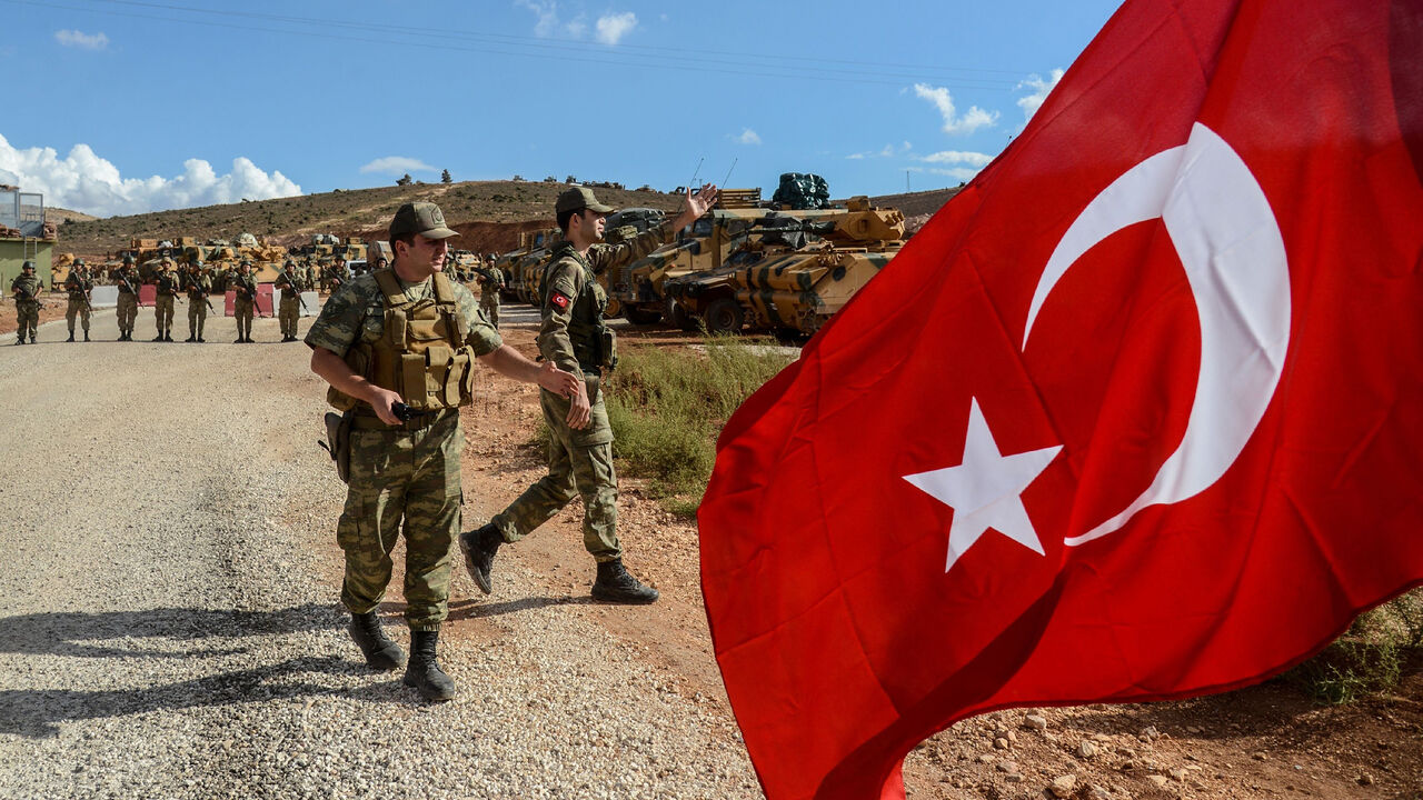 AFP_T95J2 Turkish soldiers stand near armoured vehicles as a man waves a Turkish national flag during a demonstration in support of the Turkish army's Idlib operation near the Turkey-Syria border near Reyhanli, Hatay, on October 10, 2017.
The Turkish army has launched a reconnaissance mission in Syria's largely jihadist-controlled northwestern Idlib province in a bid to create a de-escalation zone, the military said on October 9. / AFP PHOTO / ILYAS AKENGIN (Photo credit should read ILYAS AKENGIN/AFP/Getty Im