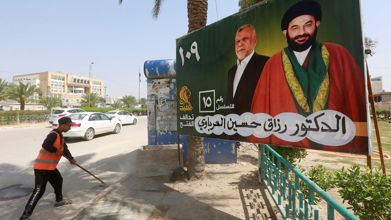 MIDEAST-CRISIS/IRAQ-ELECTION A worker cleans the street next to a campaign poster of candidates ahead of the parliamentary election, in Najaf, Iraq, April 14, 2018. REUTERS/Alaa Al-Marjani - RC155ACA6900