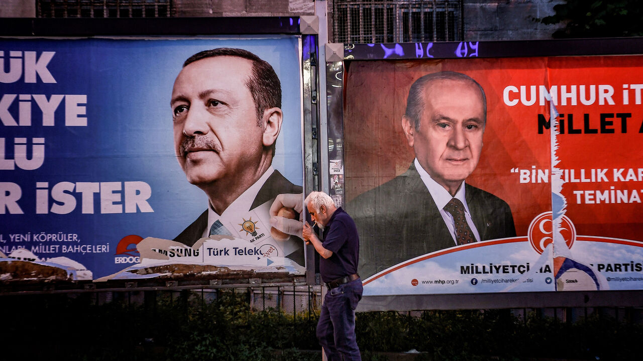 AFP_16953V A pedestrian lights a cigarette as he walks past in banners with portraits of Turrkish President Recep Tayyip Erdogan (L) and the leader of Nationalist Movement Party (MHP) Devlet Bahceli in Istanbul on June 19, 2018. - Turkey is preparing for tight presidential and parliamentary elections on June 24, while many analysts say President Erdogan wants a major foreign policy success to give him a final boost. (Photo by Aris MESSINIS / AFP) (Photo credit should read ARIS MESSINIS/AFP/Getty Images)