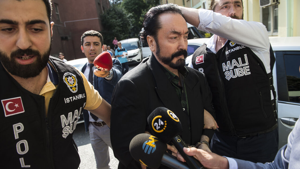 AFP_17H1KT Turkish police officers escort televangelist and leader of a sect, Adnan Oktar (C) on July 11, 2018, in Istanbul, as he is arrested on fraud charges. - Turkish police detained the televangelist on fraud charges on July 11, 2018, notorious for propagating conservative views while surrounded by scantily-clad women he refers to as his "kittens". (Photo by - / DOGAN NEWS AGENCY / AFP) / Turkey OUT (Photo credit should read -/AFP/Getty Images)