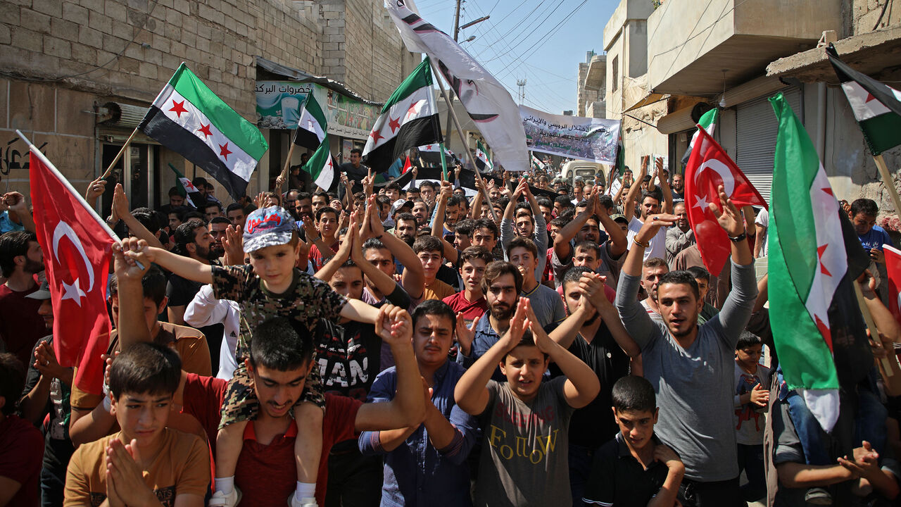 AFP_19B281 Syrians chant slogans as they wave flags of the opposition and of Turkey during a demonstration against the Syrian government in the rebel-held town of Hazzanu, about 20 kilometres northwest of the city of Idlib, on September 21, 2018. (Photo by Aaref WATAD / AFP) (Photo credit should read AAREF WATAD/AFP/Getty Images)