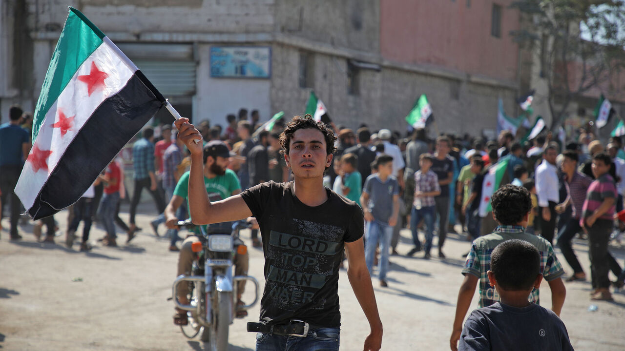 AFP_19B26W A Syrian youth waves an opposition flag during a demonstration against the Syrian government in the rebel-held town of Hazzanu, about 20 kilometres northwest of the city of Idlib, on September 21, 2018. (Photo by Aaref WATAD / AFP) (Photo credit should read AAREF WATAD/AFP/Getty Images)
