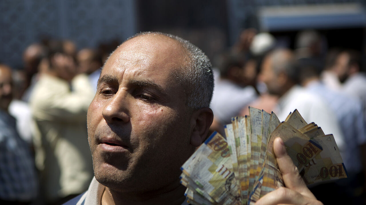 Nic6337244 A civil servant paid by the Palestinian Authority displays New Israeli Shekels (NIS) bills after he took his salary from a bank in Gaza City on June 11, 2014. Gaza's banks reopened today after being closed for six days by Hamas forces in a row over pay which was the first hitch in a reconciliation deal between Hamas and the Palestine Liberation Organisation that began with the formation of a new unity government. The PA has so far refused to pay Hamas's 50,000 civil servants, who are not registered as its e