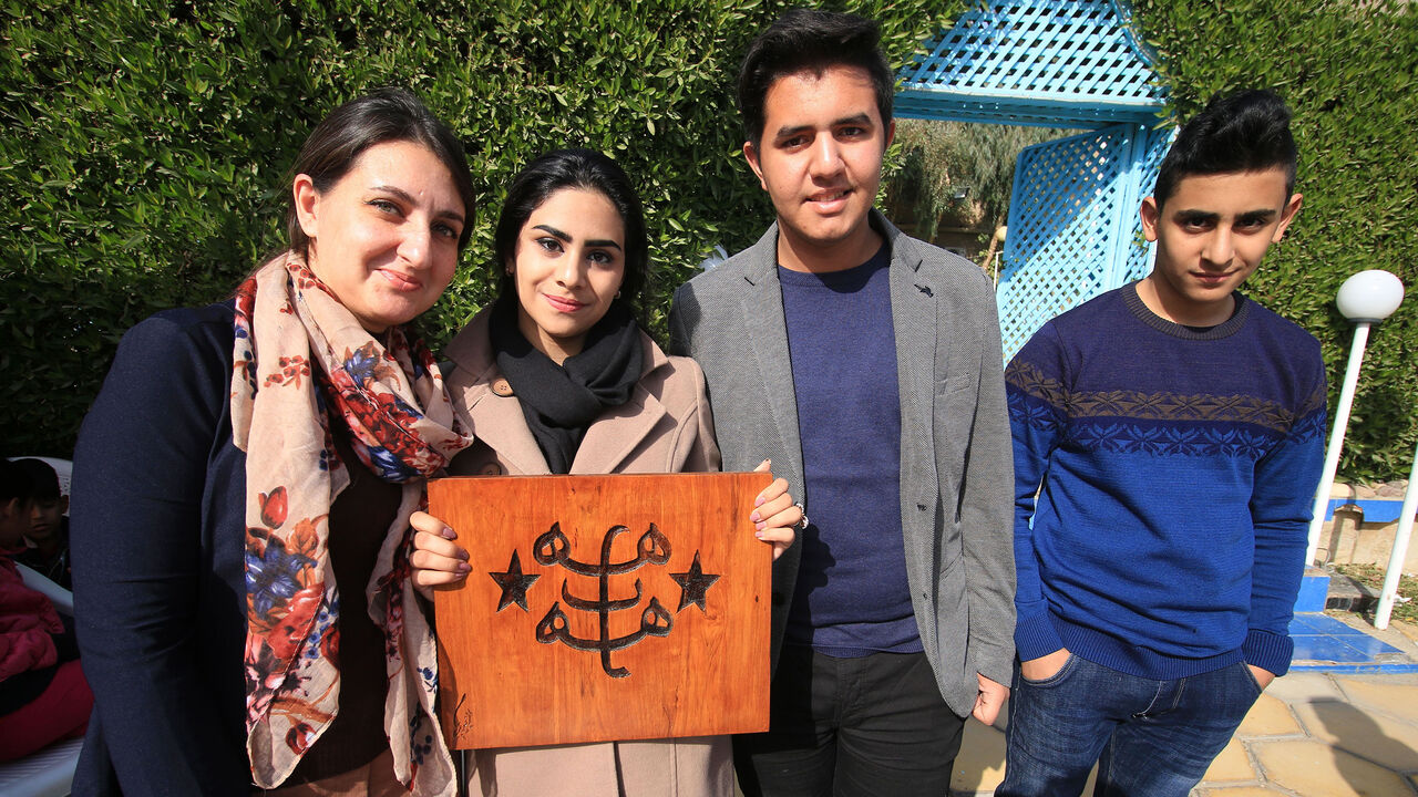 AFP_V79BB A woman poses in a group photo with a wooden cut-out depicting the ringstone symbol of the Baha'i faith during a carnival commemorating International Minority Rights Day in the southern Iraqi city of Basra on December 16, 2017. (Photo by HAIDAR MOHAMMED ALI / AFP) (Photo credit should read HAIDAR MOHAMMED ALI/AFP/Getty Images)