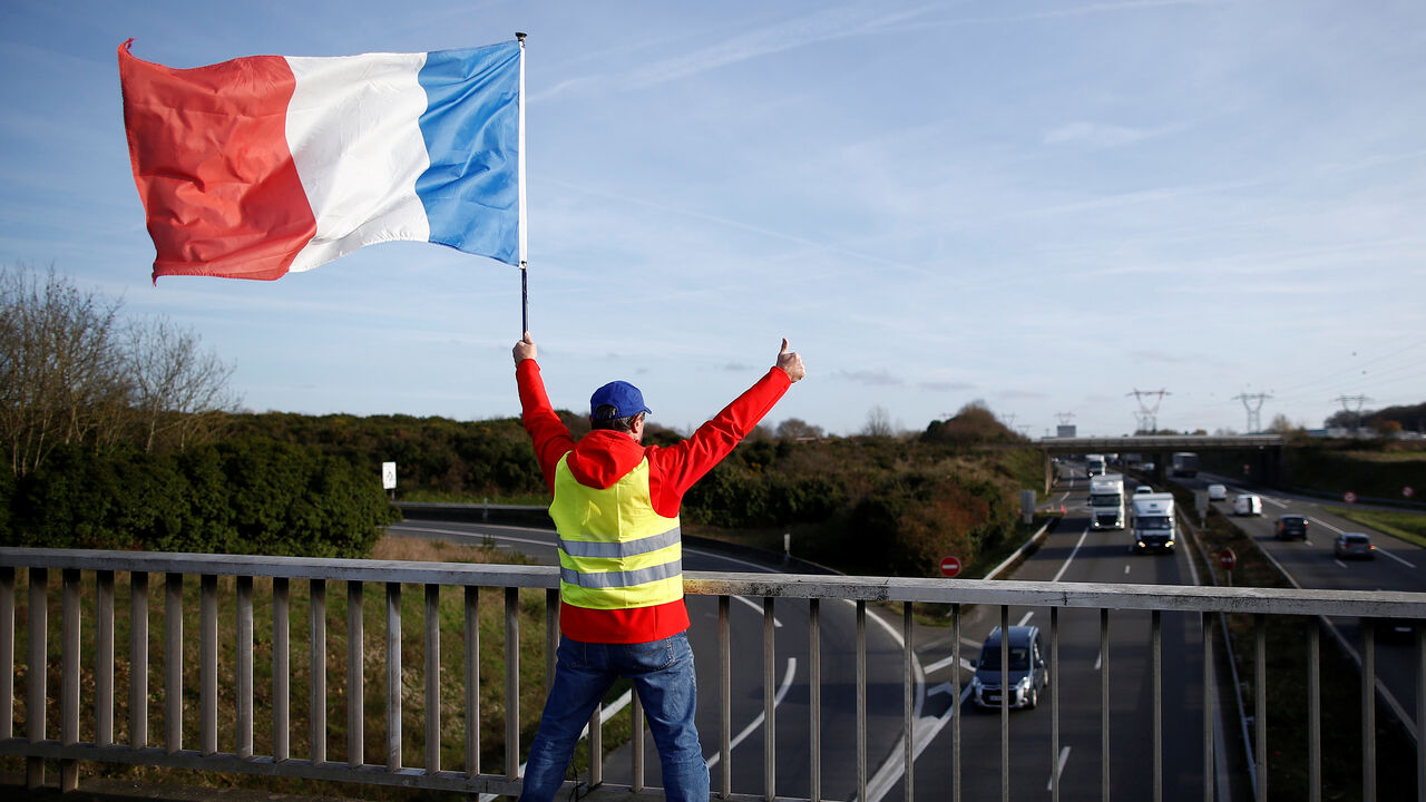 FRANCE-PROTESTS/ A man wearing a yellow vest and holding a French flag stands on a bridge near the Nantes Atlantique Airport as the "yellow vests" movement continues, in Bouguenais, France, December 11, 2018. REUTERS/Stephane Mahe - RC1FB4AA8210