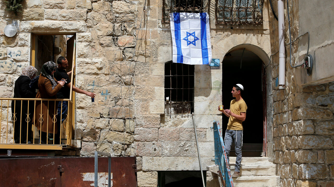 An Israel flag is seen hanging on a house as an Israeli settler looks at Palestinians in Hebron, in the occupied West Bank An Israel flag is seen hanging on a house as an Israeli settler looks at Palestinians in Hebron, in the occupied West Bank March 27, 2018. REUTERS/Mussa Qawasma TPX IMAGES OF THE DAY - RC13D45CEAE0