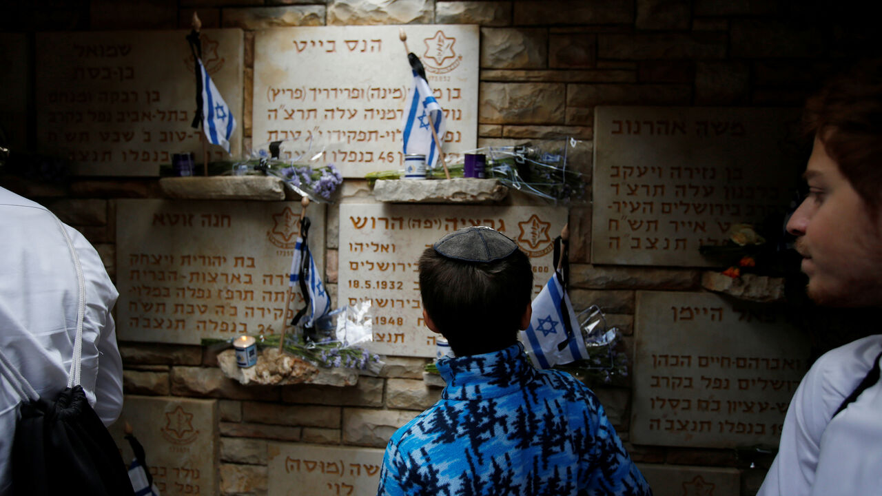 ISRAEL-MEMORIAL DAY/ A youth looks at flowers and flags laid next to tombstones on Memorial Day, when Israel commemorates it's fallen soldiers, at Mount Herzl military cemetery in Jerusalem May 8, 2019. REUTERS/Ronen Zvulun - RC1C955B89F0