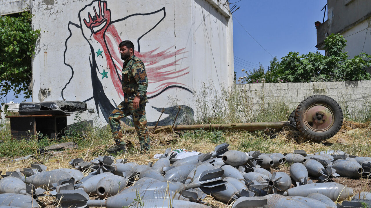 1144239265 A Syrian government soldier walks past strewn mortar shells in the village of Qalaat al-Madiq, some 45 kilometres northwest of the central city of Hama, on May 17, 2019. - Syrian government forces a week prior had recaptured the northwestern town on the southwestern edge of the jihadist-controlled Idlib region, from around which jihadists and allied rebels were launching rockets on their Russian ally's key airbase. The capture of the town of Qalaat al-Madiq comes after weeks of intensified air strikes and s
