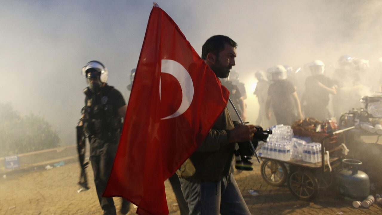 TURKEY-PROTESTS/ A protester holds a Turkish flag as riot police order them to evacuate Gezi Park in central Istanbul June 15, 2013. Thousands of people took to the streets of Istanbul overnight on Sunday, erecting barricades and starting bonfires, after riot police firing teargas and water cannon stormed a park at the centre of two weeks of anti-government unrest. Lines of police backed by armoured vehicles sealed off Taksim Square in the centre of the city as officers raided the adjoining Gezi Park late on Saturday, where
