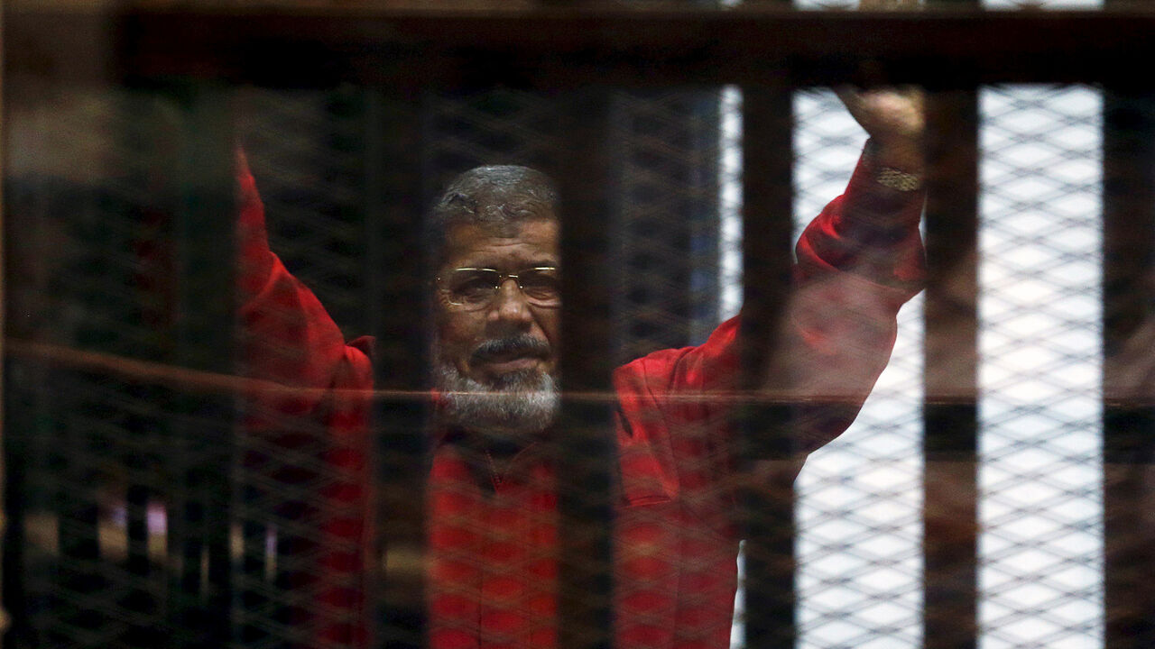 EGYPT-COURT/ Deposed President Mohamed Mursi greets his lawyers and people from behind bars at a court wearing the red uniform of a prisoner sentenced to death, during his court appearance with Muslim Brotherhood members on the outskirts of Cairo, Egypt, June 21, 2015. REUTERS/Amr Abdallah Dalsh/File Photo - S1AETCRHIPAB