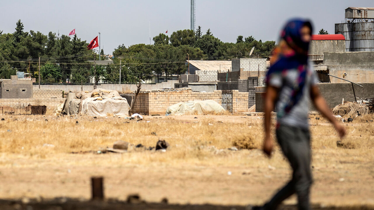 1160482134 A Syrian Kurd walks during a protest and sit-in against Turkey, in the town of Ras al-Ain in Syria's Hasakeh province near the Turkish border on August 9, 2019, with the flags of Turkey seen across the border in the background. (Photo by Delil SOULEIMAN / AFP) (Photo credit should read DELIL SOULEIMAN/AFP/Getty Images)
